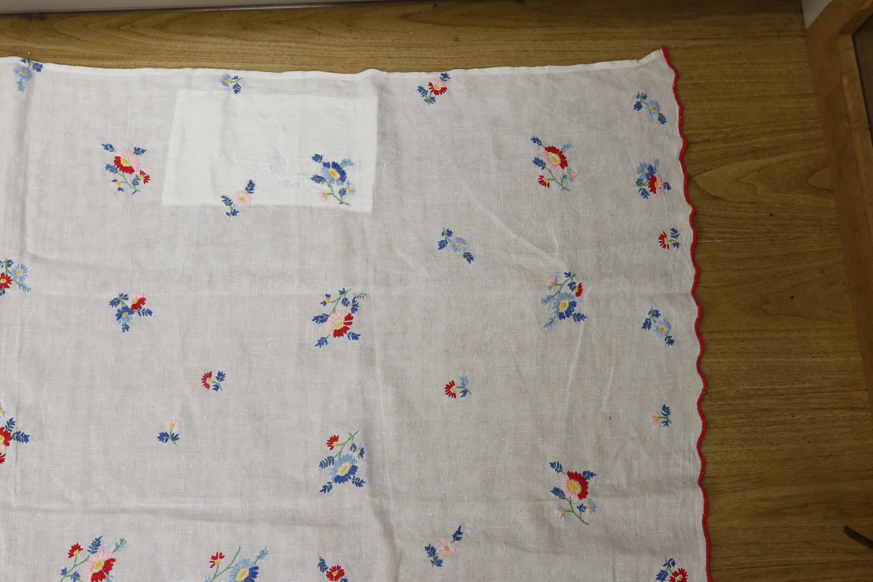 A 20th century woven linen panel, hand embroidered with scattered floral polychrome sprigs and a scalloped red buttonholed embroidered edge, possibly Swiss, 153 x 100cm